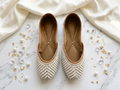 Cream pearl beaded chevron Punjabi jutti pair, top-down view on marble and silk background