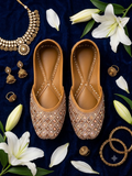 Mustard and bronze diamond sequin jutti - top-down flat lay on navy blue velvet with gold jewelry and lilies