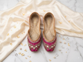 Pink mirror work bridal Punjabi jutti pair, top-down view on marble and silk background